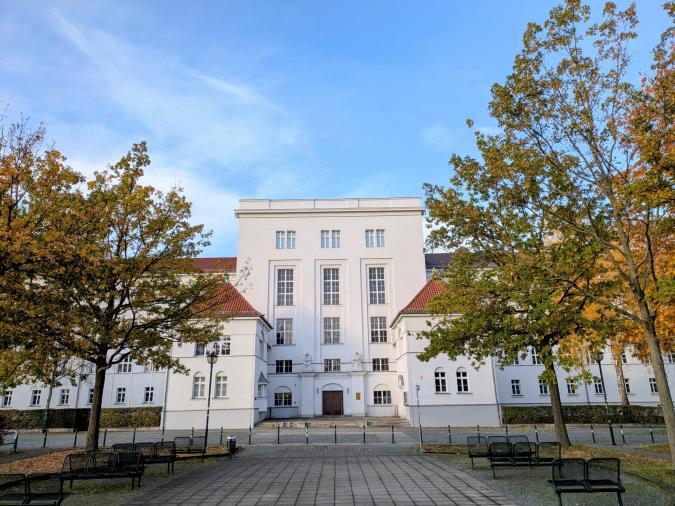 Blick auf den Haupteingang des Schulgebäudes, umrahmt von herbstlichen Bäumen, bei blauem Himmel