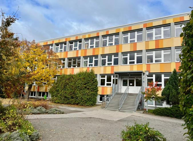Blick auf den herbstlichen Schulhof und die bunte Fassade des Schulgebäudes, bei blauen Himmel