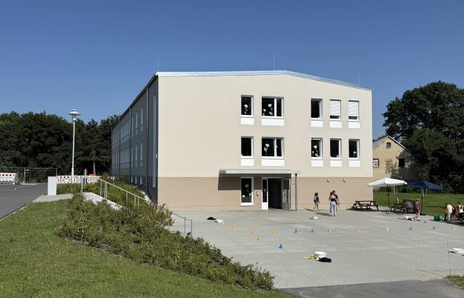 modernes helles Schulgebäude mit Kindern auf der Freifläche vor dem Eingang