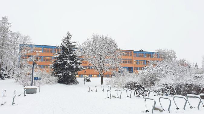 Blick auf das verschneite Schulgebäude von der Straße aus.