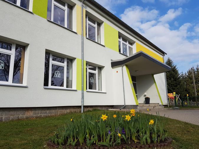 Hier sieht man den Haupteingang. Davor befindet sich ein Blumenbeet mit Frühblühern.