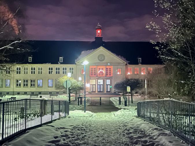Blick auf das verschneite Schulgebäude bei Nacht von der Brücke aus.