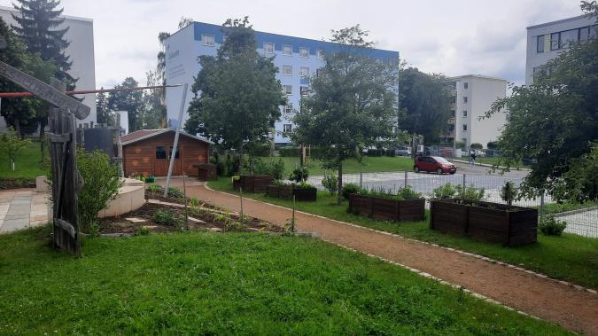 Blick in den Schulgarten mit Hochbeeten, Wegen, grünes Klassenzimmer und Gartenaus.