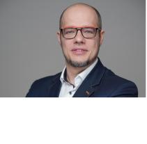 Michael Theiss, schwarze kurze Haare, Halbglatze, dunkle Brille, blaues Jackett und weißes Hemd